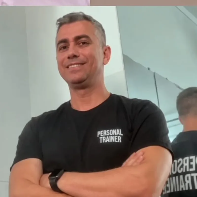 Wagner Menon, personal trainer, sorrindo de braços cruzados com camiseta Personal Trainer